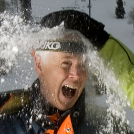 laughing man with gray hair with someone out of frame throwing snow on his head